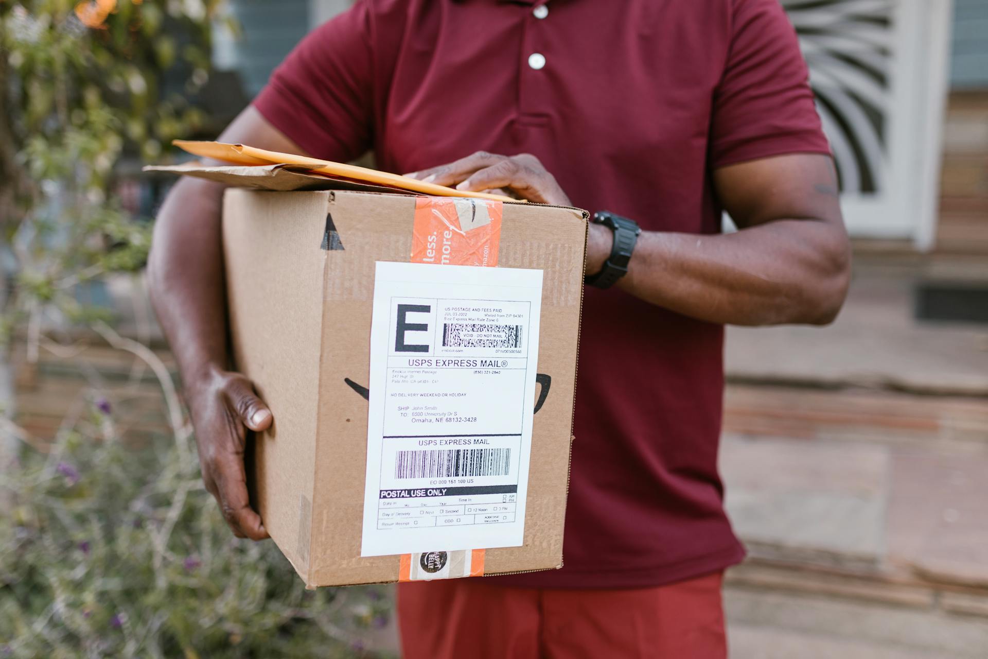 Delivery man in maroon uniform holding a package with a visible shipping label.